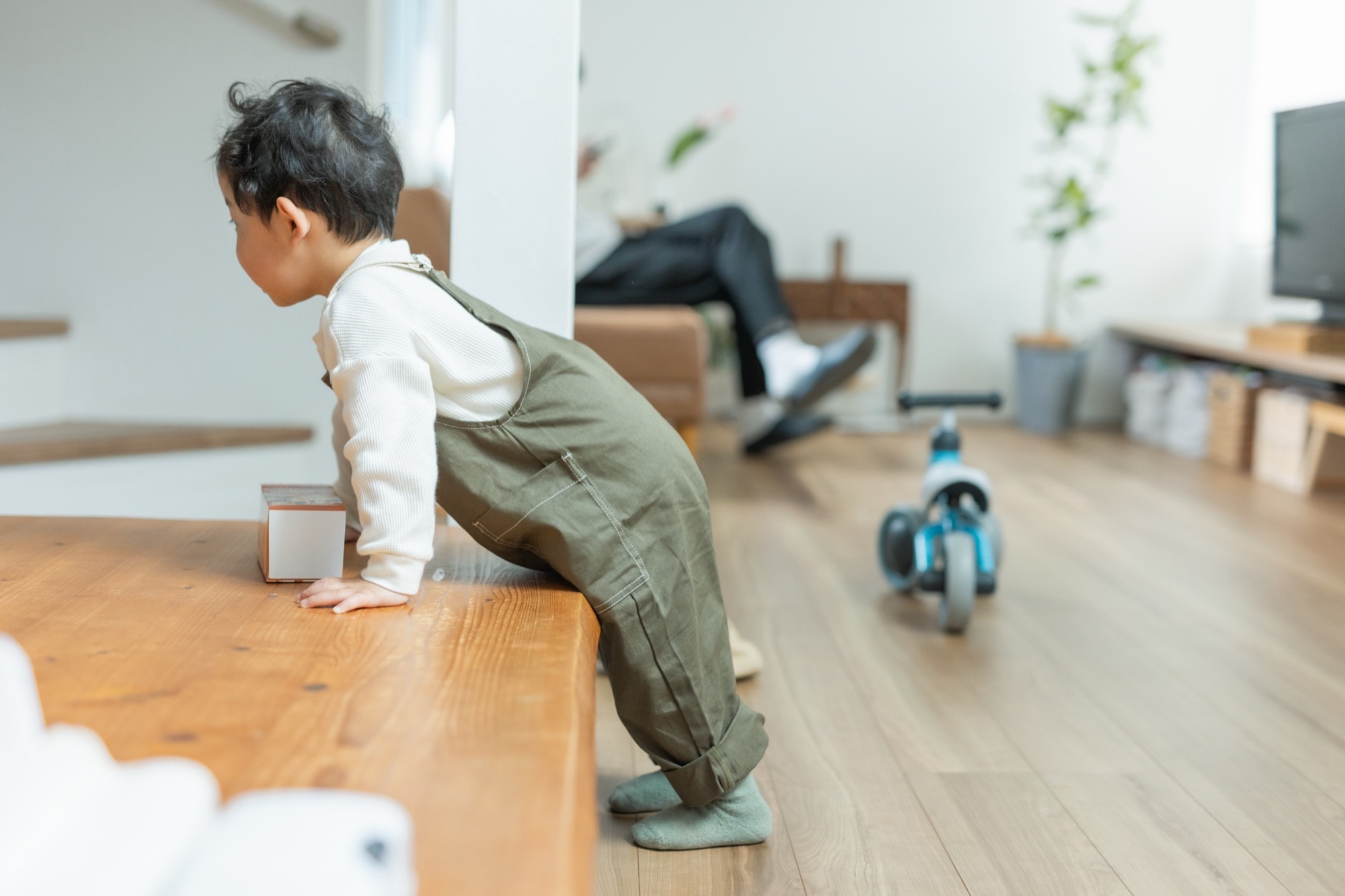 リビングで階段に手を付く日本人の男の子の横顔と後ろでくつろぐ父親